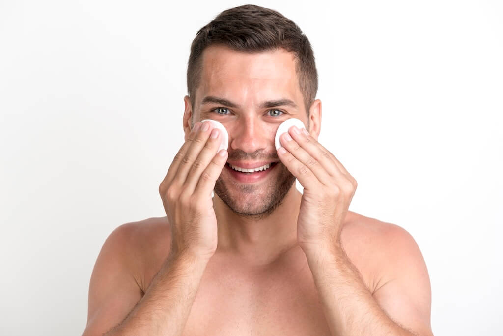 pulizia viso perfetta uomo che deterge il suo viso con i cuscinetti di cotone