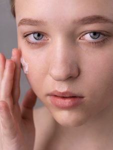 pelle spenta opaca donna che applica fluido solare viso spf50